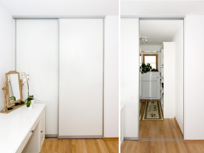 Zwei weiße Schiebetüren trennen eine Nische vom Raum ab und ermöglichen die Nutzung als begehbaren Kleiderschrank