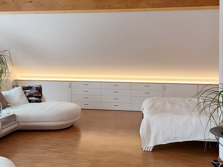 Lange Kommode mit Schubladen und Schiebetüren in der Dachschräge. In der Deckplatte ist eine indirekte Beleuchtung zur Decke eingebaut.